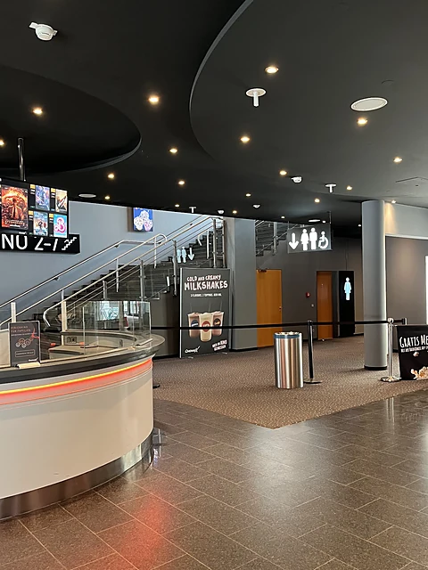 Kinofoyer mit geschwungener Snacktheke, Treppe zu den Sälen und Anzeigetafeln mit Filmplakaten