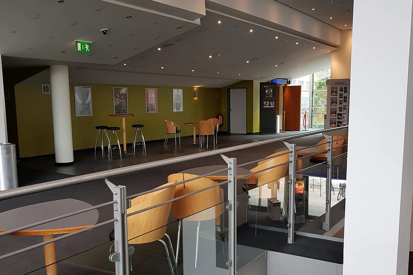 Obergeschoss im Kinofoyer mit Stehtischen, Hockern, gerahmten Filmplakaten an olivgrüner Wand und Geländer