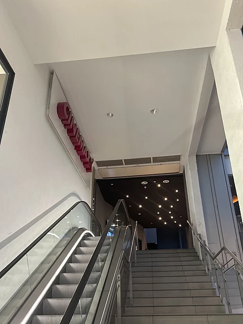 Rolltreppe und Treppe führen zu einem Durchgang mit rotem CinemaxX-Schriftzug an der Wand