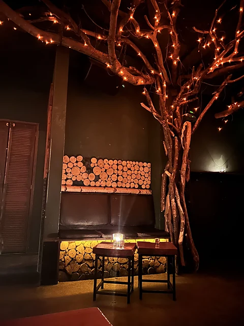 Baum mit Lichterketten im Gastraum der clockers Bar, daneben eine Wand aus gestapelten Holzscheiten