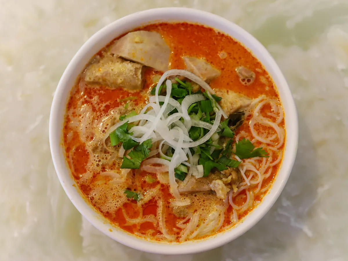 Schale mit vietnamesischem Curry, Reisnudeln, Fleisch, Koriander und Zwiebelringen