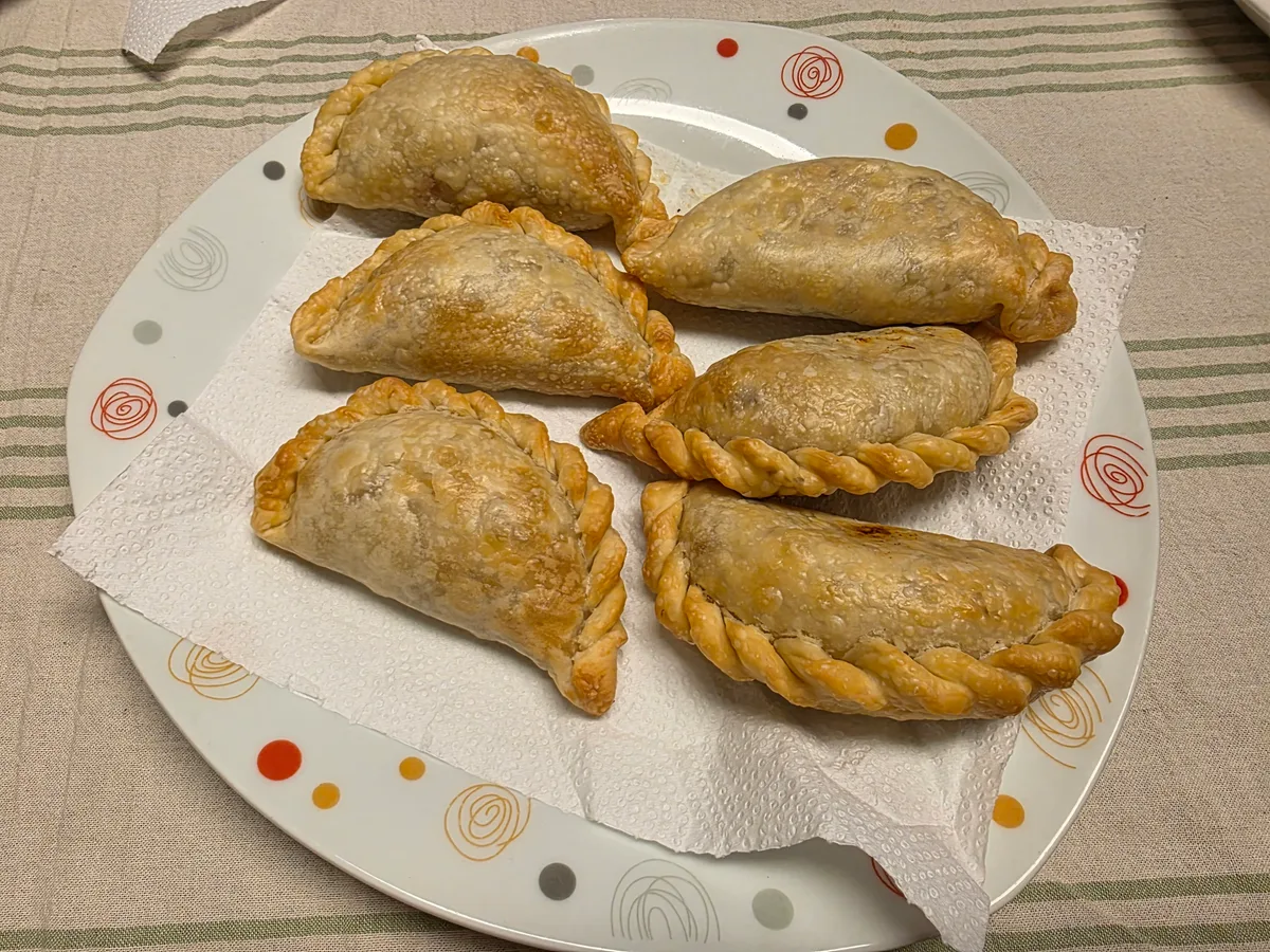 Sechs goldbraun gebackene Empanadas auf einem weißen Teller