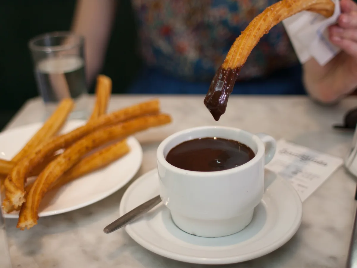 Churros werden in eine Tasse mit dunkler Schokolade getaucht