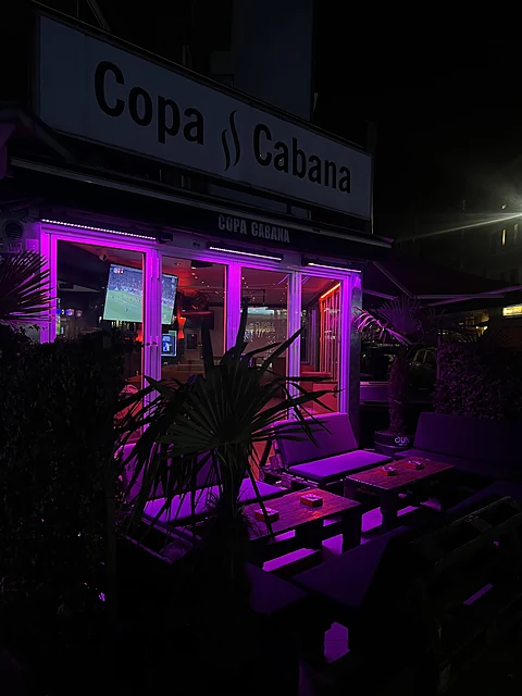 Eingang der Copa Cabana Bar bei Nacht mit Schild, Palme und violettem Licht