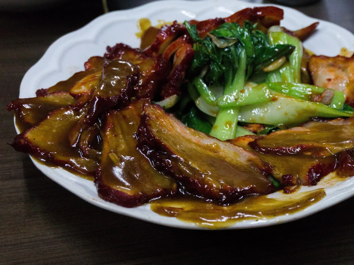 Glasierte Scheiben kantonesischen Schweinebratens mit Pak Choi auf einem weißen Teller