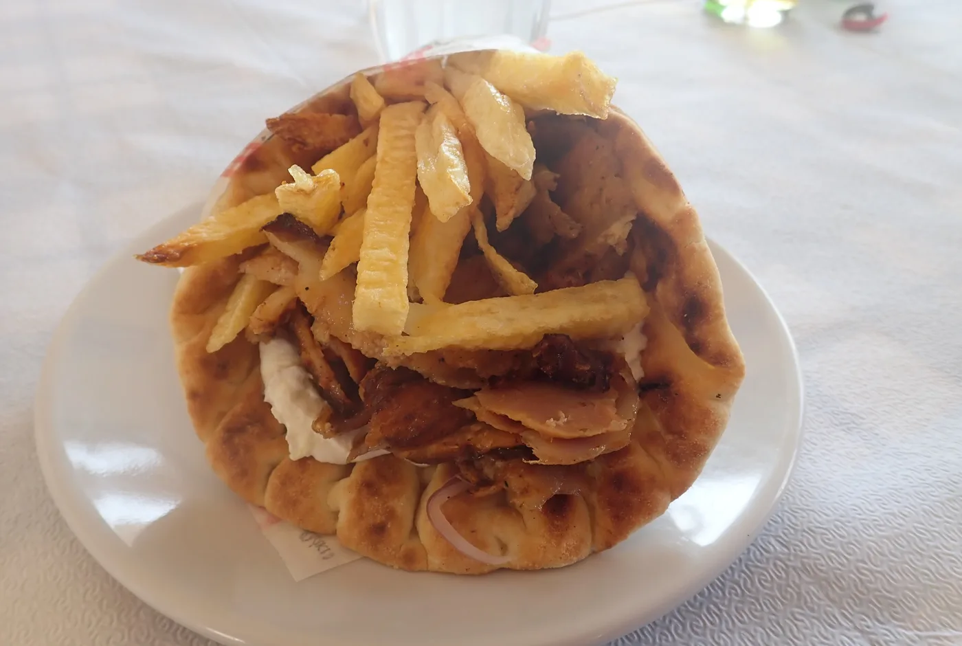 Gyros mit Pommes und Zaziki in einem Pitabrot auf einem weißen Teller