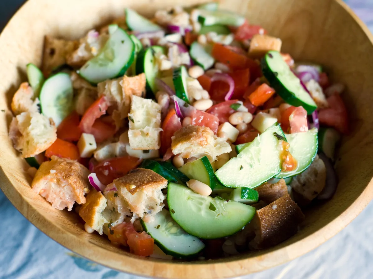 Brotsalat mit Tomaten, Gurken, roten Zwiebeln und weißen Bohnen in einer Holzschale