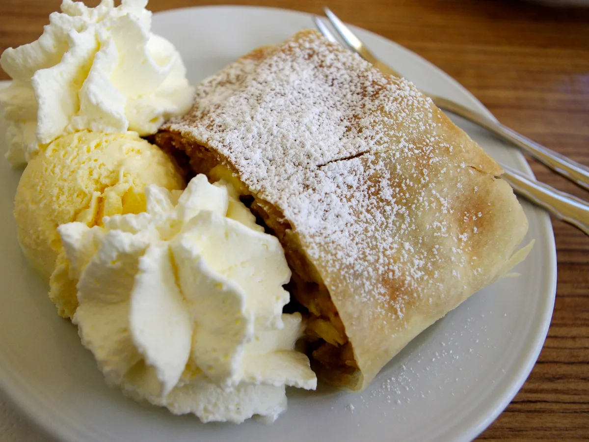 Strudel mit Puderzucker, daneben eine Kugel Vanilleeis und Schlagsahne