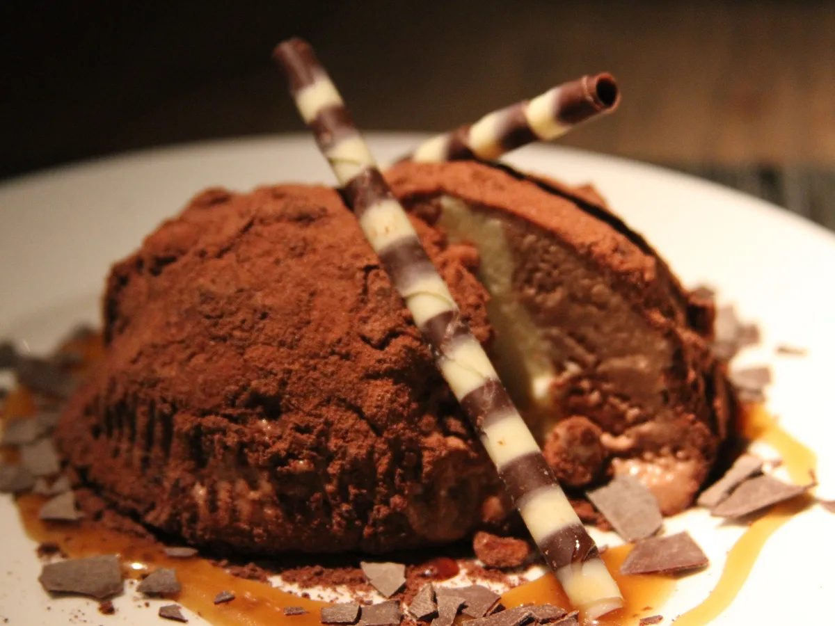 Tartufo mit Kakaopulver, Schokoladenröllchen und Schokoladensplittern auf einem weißen Teller
