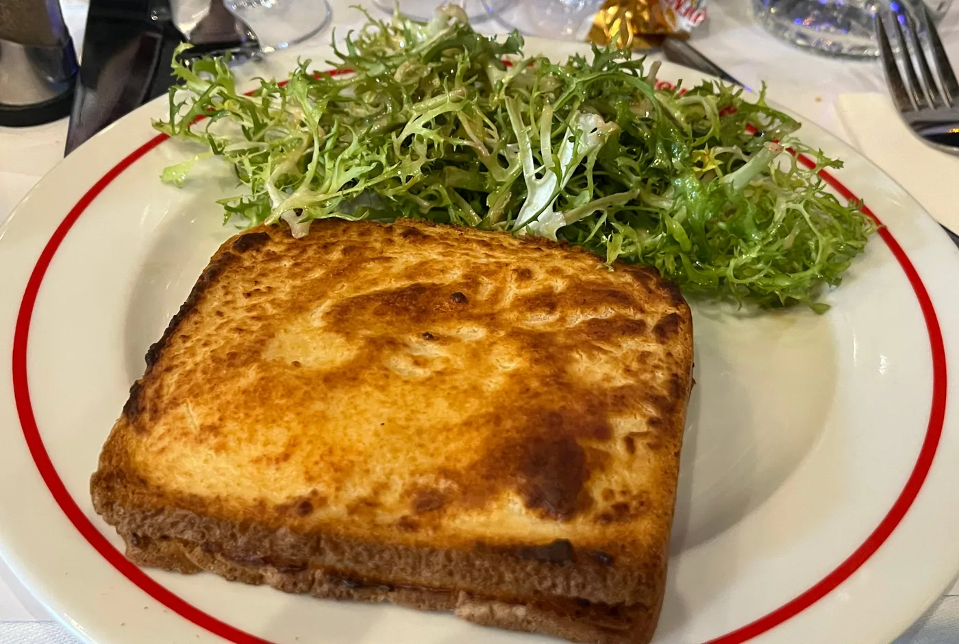 Goldbraun überbackenes Croque Monsieur mit Blattsalat auf einem weißen Teller
