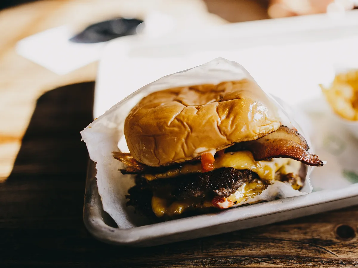 Cheeseburger mit Speck und geschmolzenem Käse in Papier auf einem Metalltablett