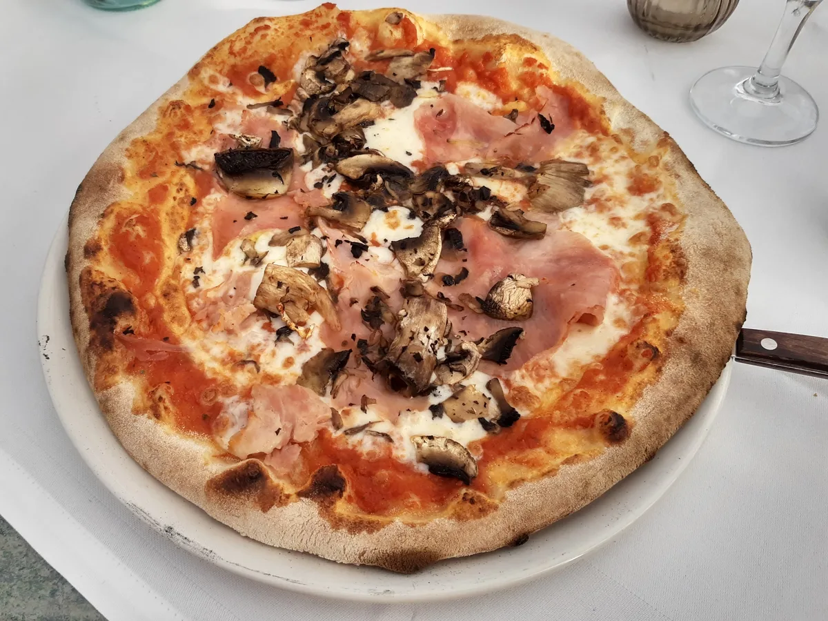 Runde Pizza mit Schinken und Champignons auf einem weißen Teller