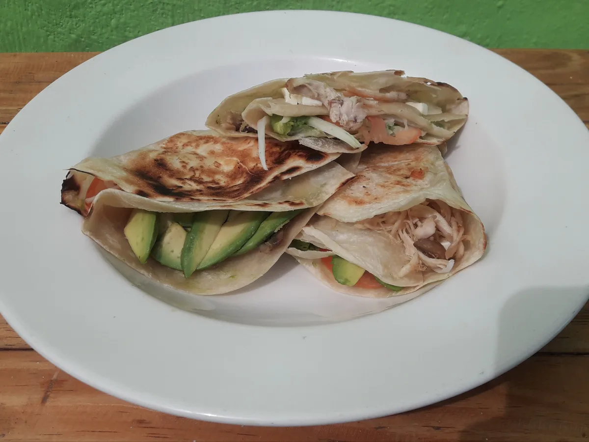 Drei gefüllte Wraps mit Hähnchen, Avocado und Gemüse auf einem weißen Teller