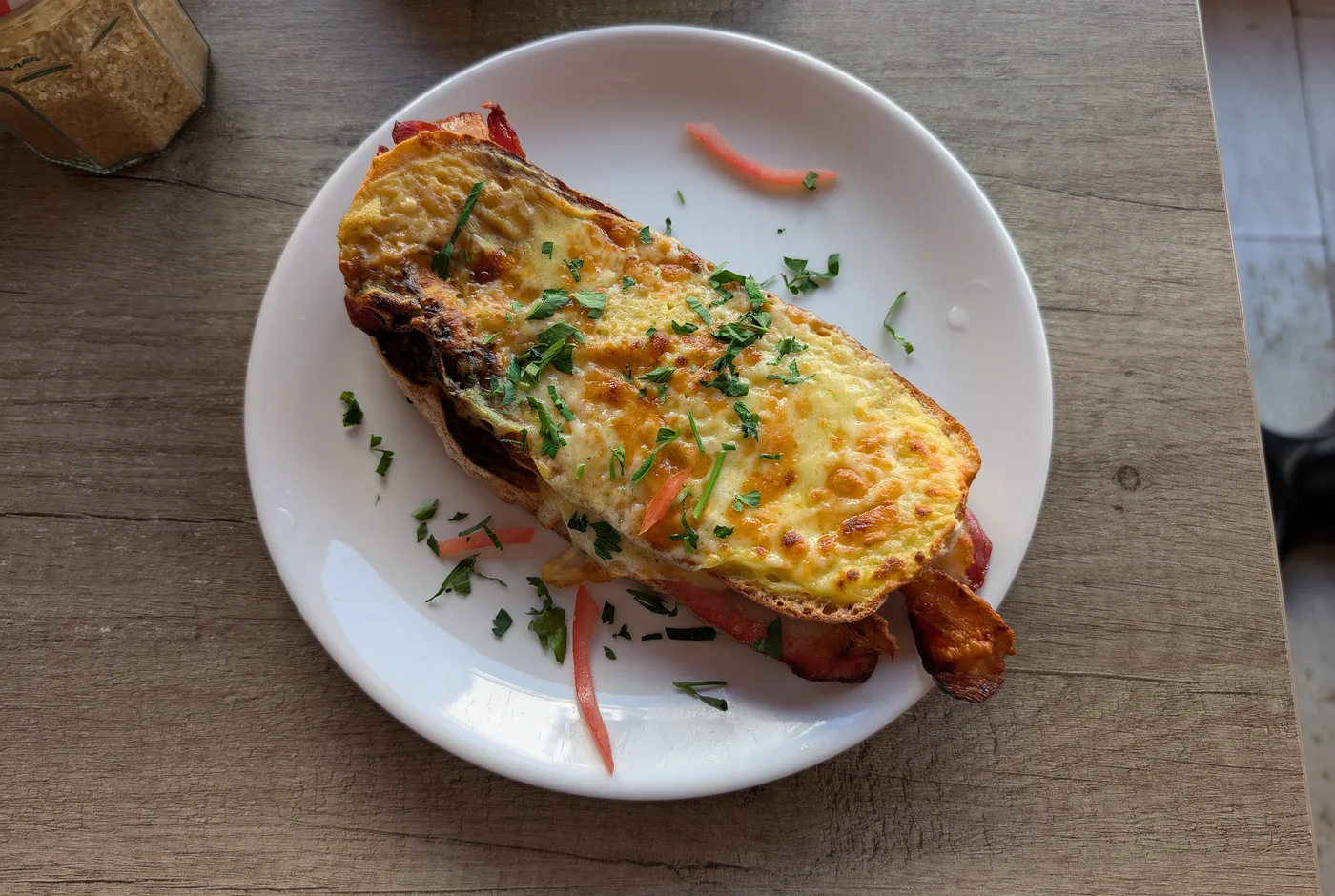 Überbackenes Croque mit geschmolzenem Käse, Speck und Petersilie auf einem weißen Teller