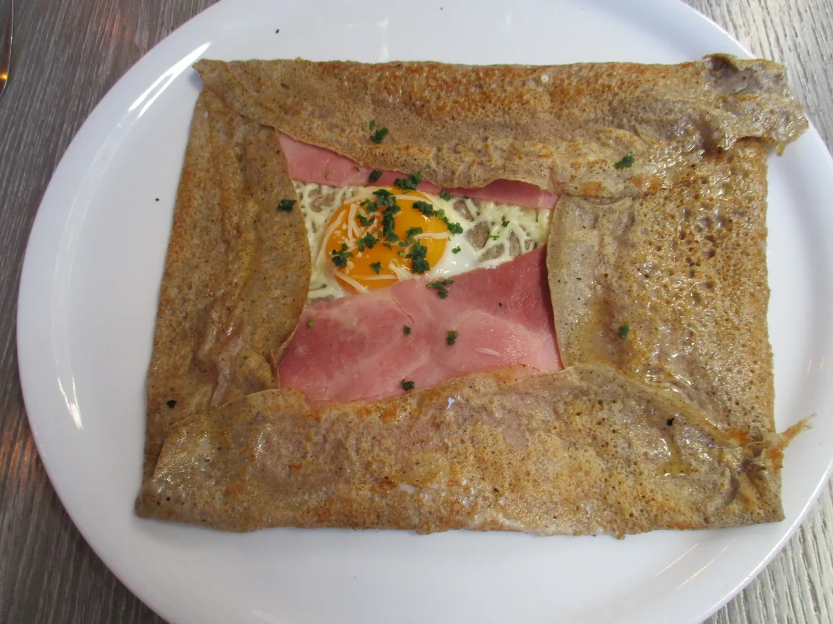 Herzhafte Crêpe mit Schinken, Käse und Spiegelei, an den Seiten eingeschlagen, auf einem weißen Teller
