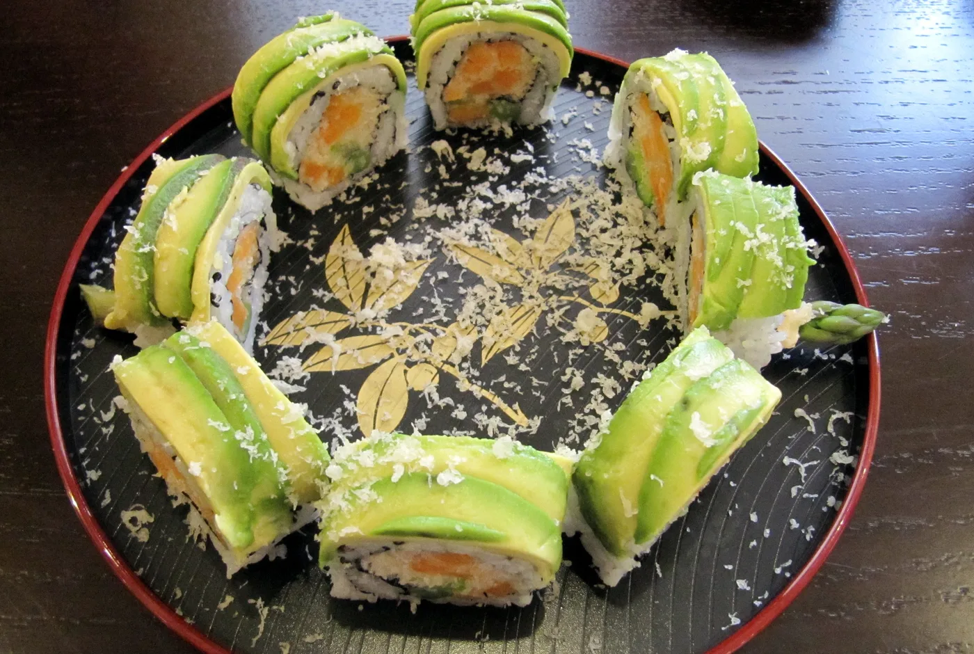 Sushirollen mit Avocadoscheiben belegt, auf einem schwarzen Teller im Kreis angerichtet