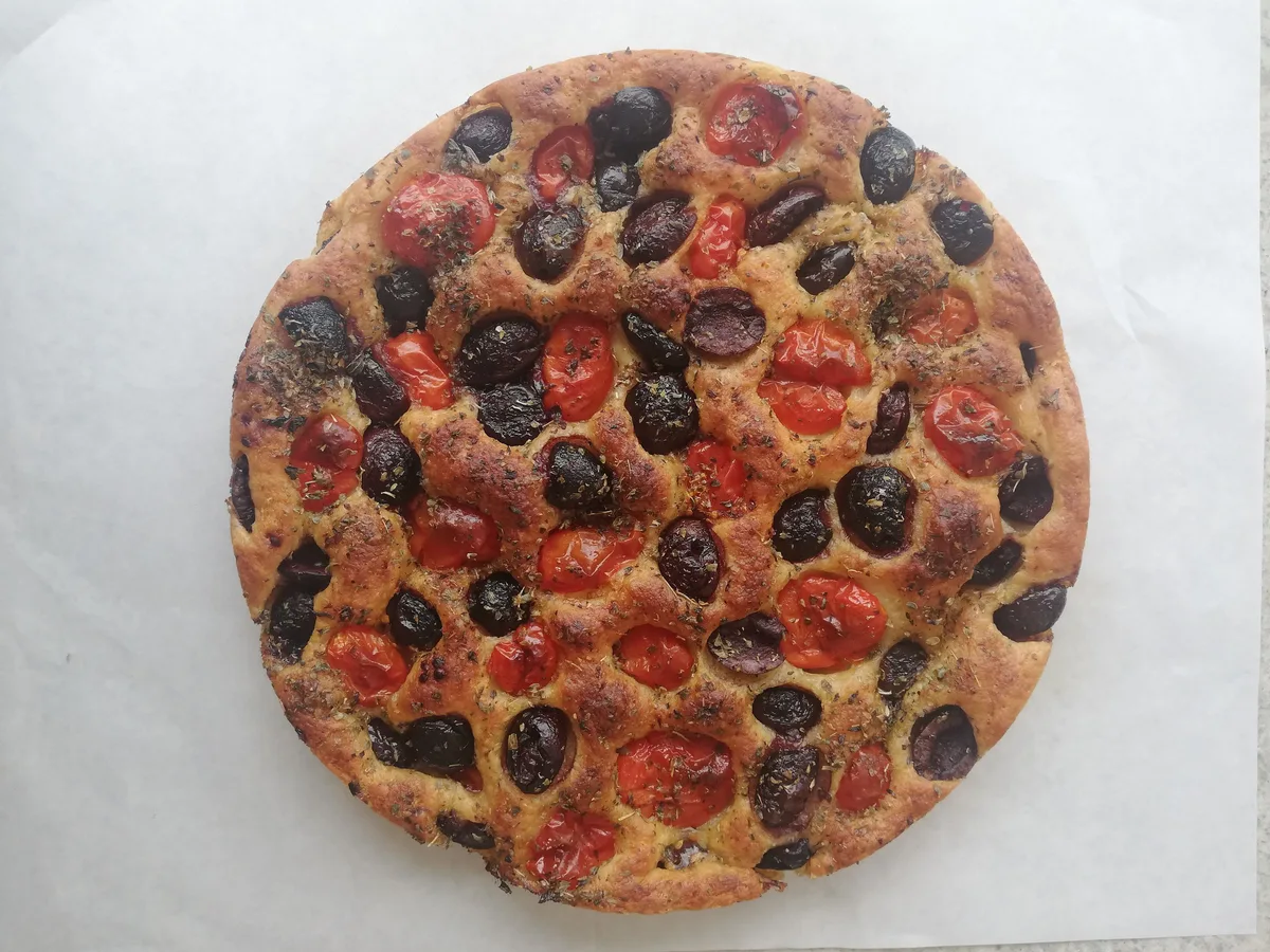 Runde Focaccia mit Kirschtomaten, Oliven und Oregano auf Backpapier