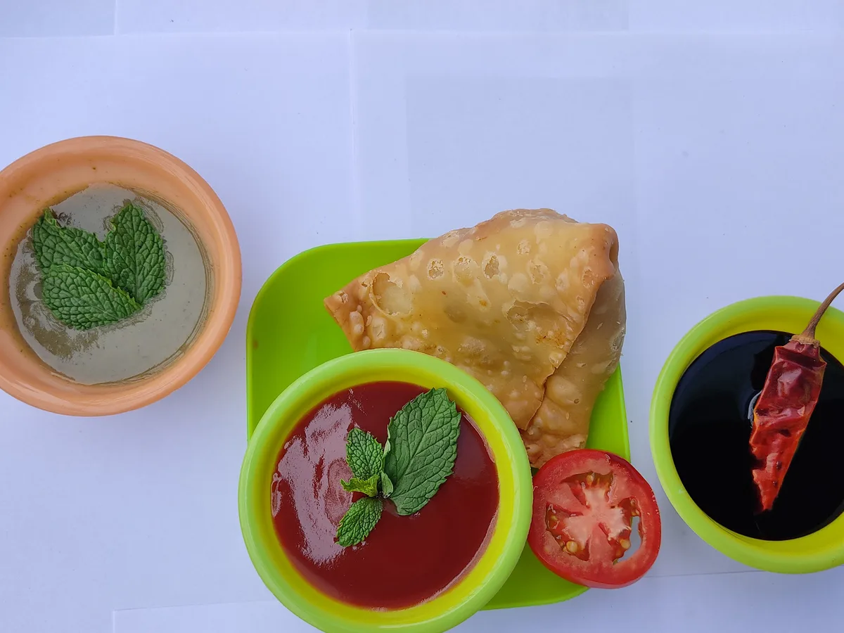 Frittierte Samosa neben Schälchen mit Minz-, Tomaten- und Tamarindensauce