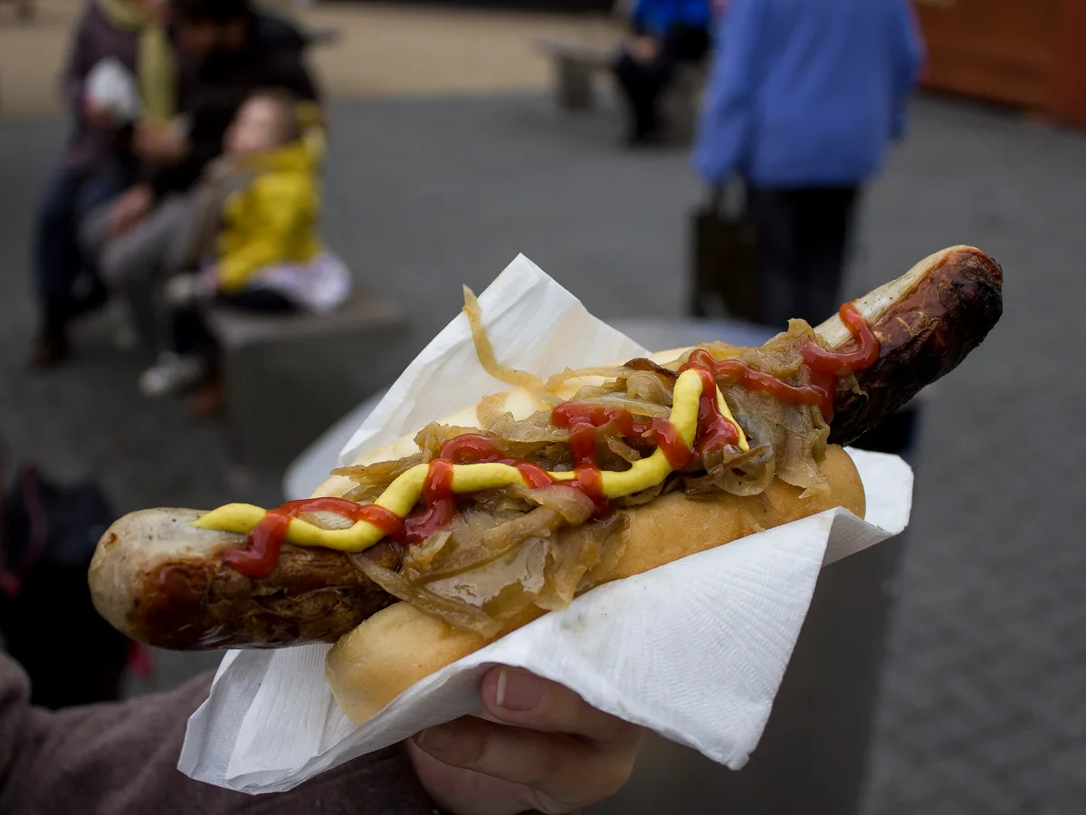 Gegrillte Bratwurst im Brötchen mit Röstzwiebeln, Senf und Ketchup