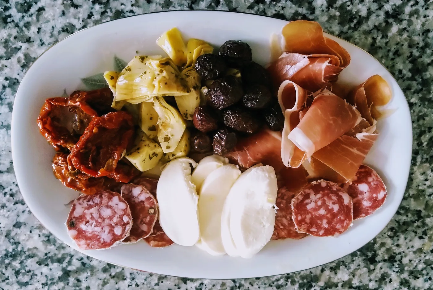 Vorspeisenplatte mit Schinken, Salami, Mozzarella, Artischocken, Oliven und getrockneten Tomaten