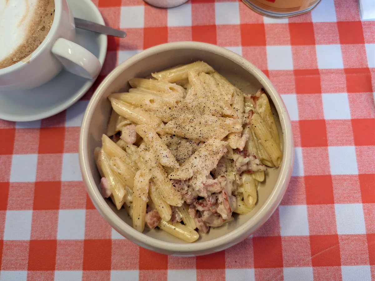 Schale mit Nudeln in heller Sauce, Speckwürfeln und Pfeffer auf einer rot karierten Tischdecke