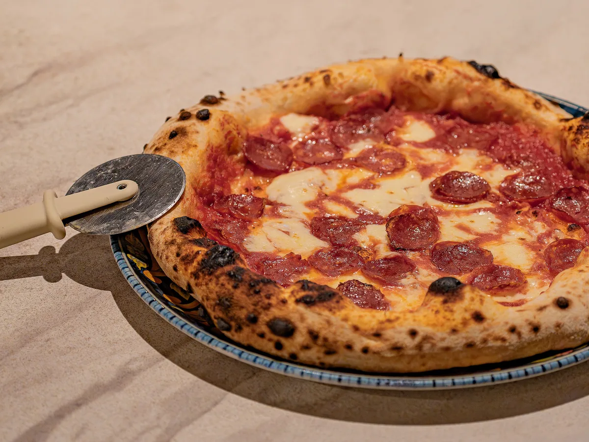 Große Pizza mit Salami und Mozzarella, die über den Tellerrand hinausragt