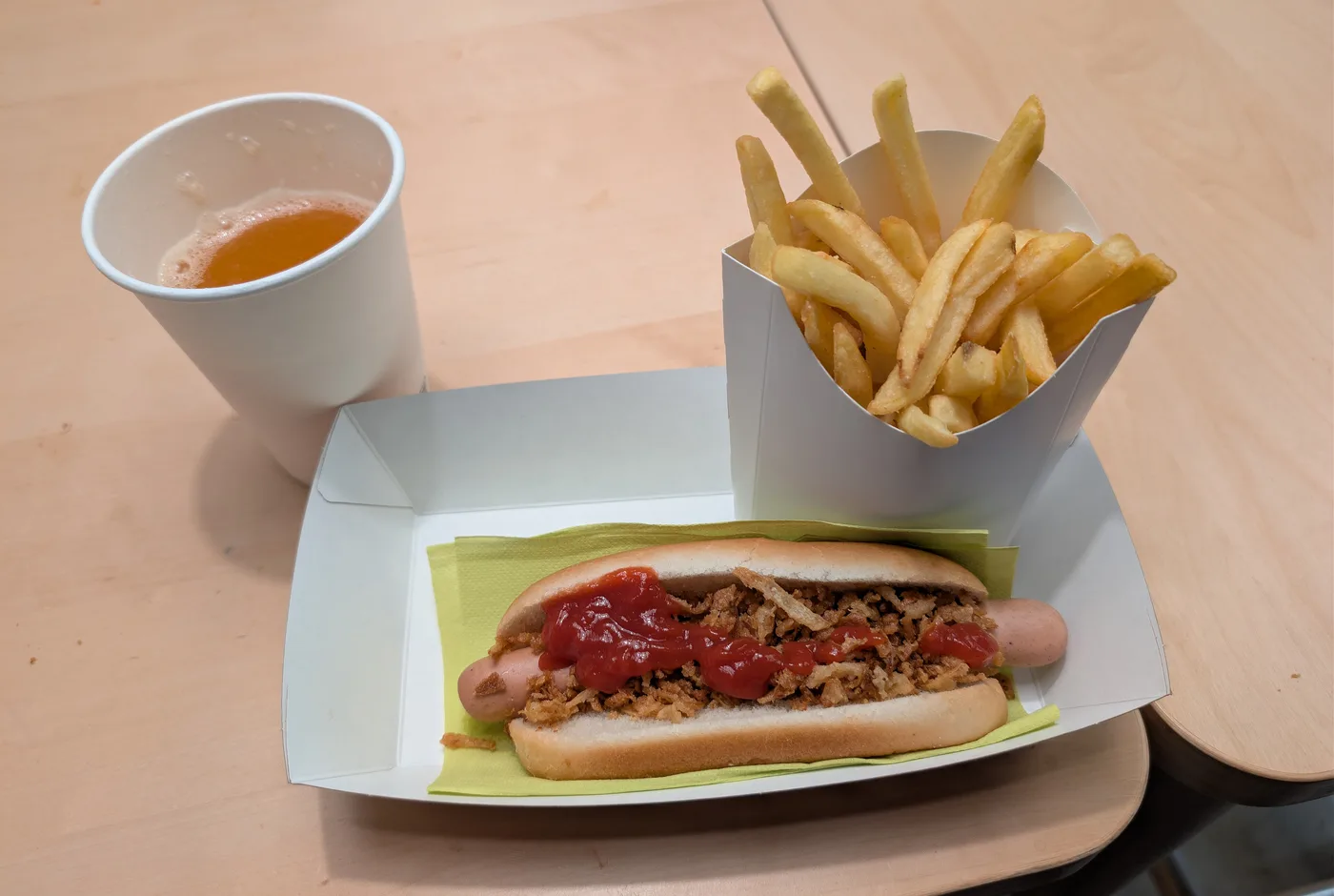 Hotdog im weichen Brötchen mit Röstzwiebeln und Ketchup, daneben eine Tüte Pommes