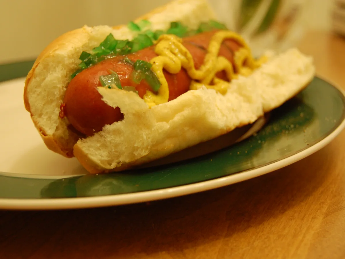 Hotdog im Brötchen mit Senf und klein geschnittenen eingelegten Gurken