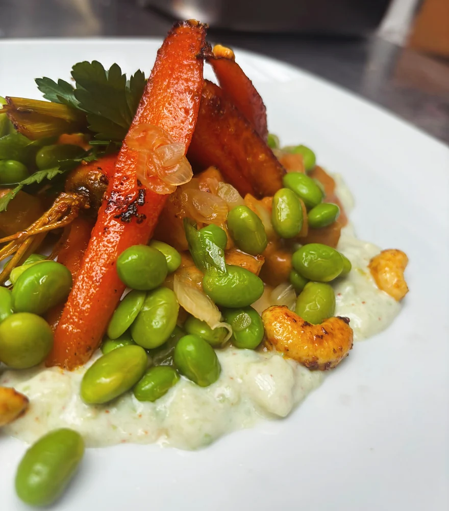 Geschmorte Karotten mit Edamame, Cashews und Avocado-Sojajoghurt auf weißem Teller