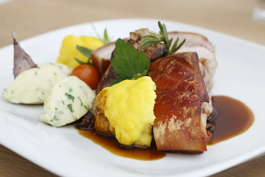 Gebratener Schweinebauch mit Kartoffelpüree, Polenta und Rotweinjus auf weißem Teller