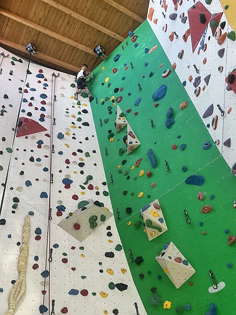Hohe Kletterwand in Weiß und Grün mit bunten Griffen, Umlenkpunkten und herabhängenden Seilen