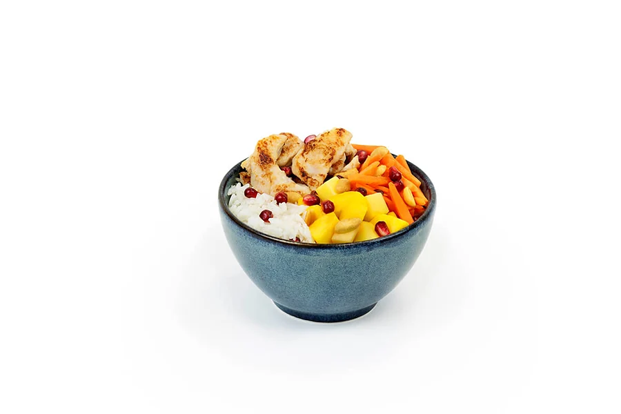 Kleine Bowl mit Hähnchen, Mango, Karotte und Granatapfelkernen in dunkler Schale