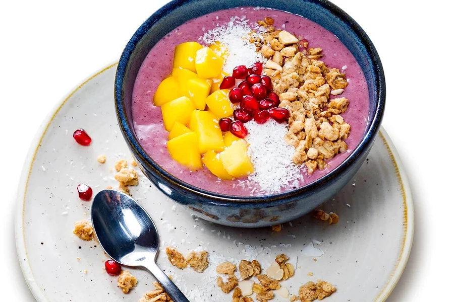 Açaí-Bowl mit Mango, Granatapfel, Kokosraspeln und Granola in dunkler Schale