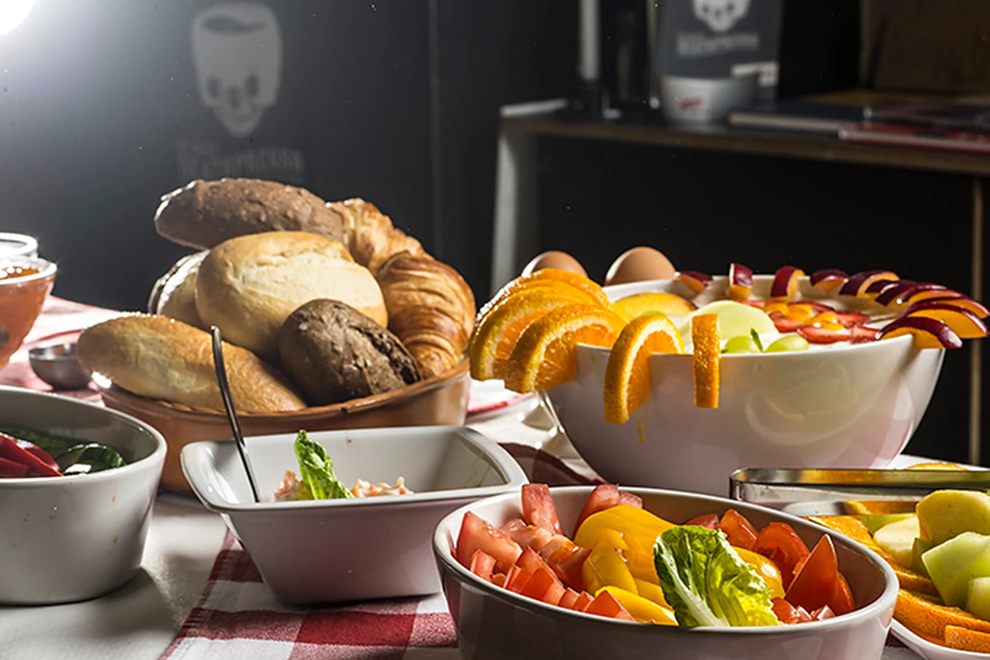 Gedeckter Tisch mit Brötchenkorb, Croissants, Obstschalen und Aufschnitt, im Hintergrund das Totenkopf-Logo