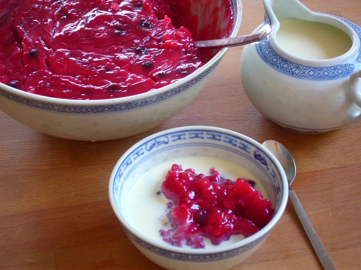Rote Grütze mit Vanillesoße in einer Schale, daneben ein Kännchen