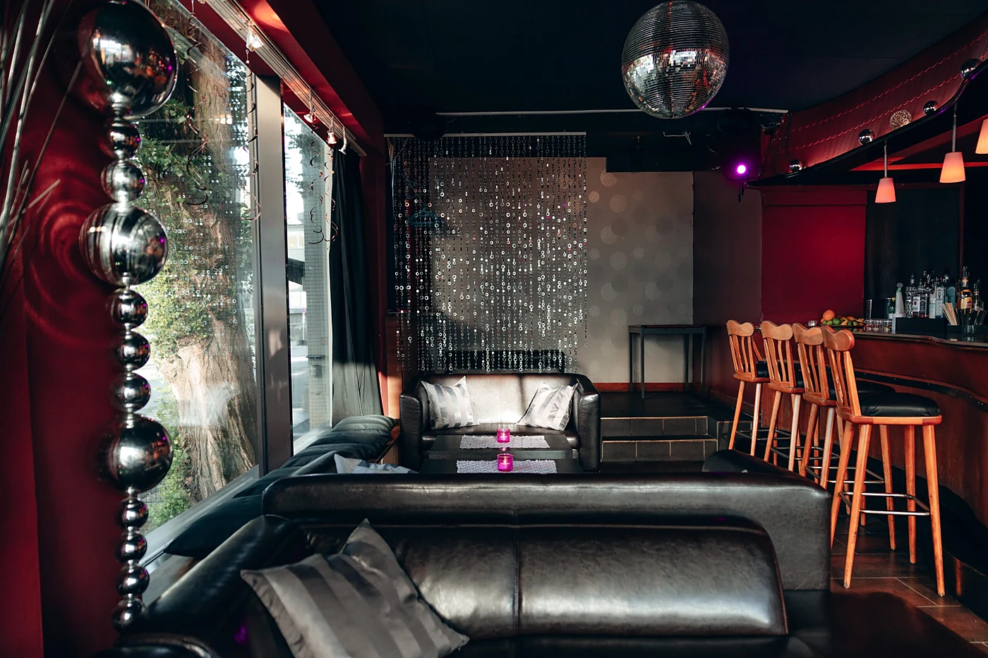 Lounge mit schwarzen Ledersofas, Glitzervorhang, Discokugel und Barhockern am Tresen