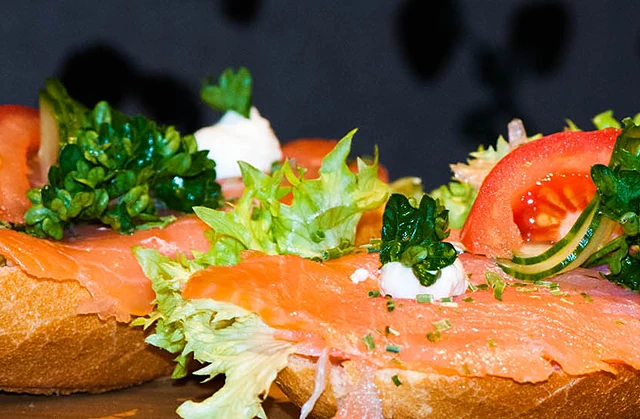 Zwei Baguettehälften mit Räucherlachs, Salat, Tomate, Gurke und Frischkäse-Tupfern