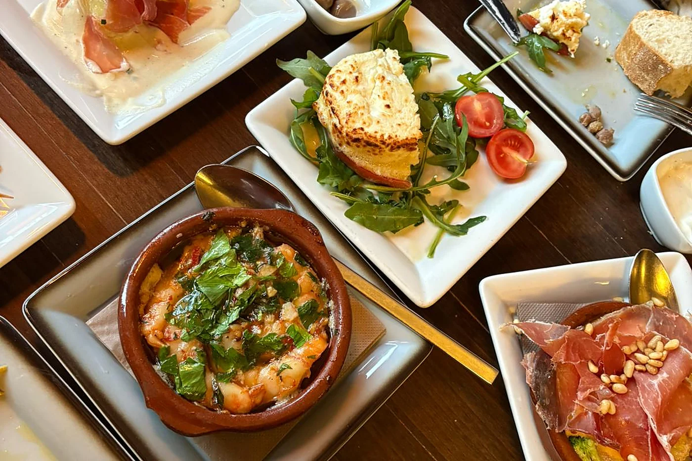 Mehrere Tapas auf dem Tisch: Gambas in der Tonschale, gratinierter Ziegenkäse auf Rucola und Serranoschinken