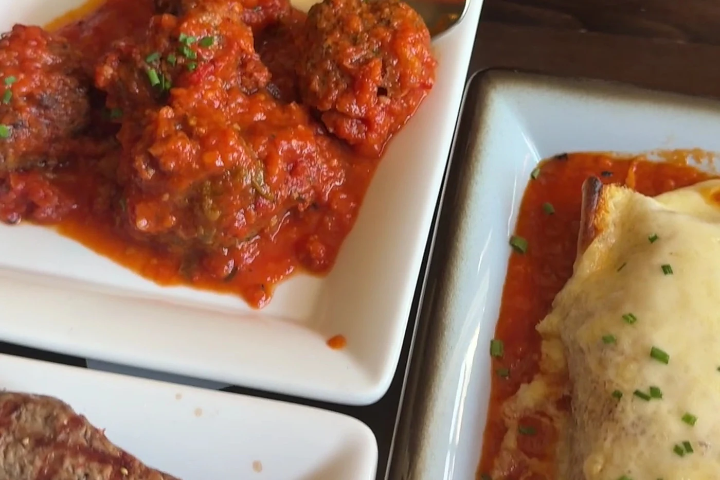 Albóndigas in Tomatensauce, gegrilltes Fleisch und ein Gratin auf weißen Tapastellern