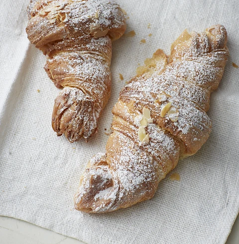 Zwei Mandelcroissants mit Puderzucker und Mandelblättchen auf weißem Leinen
