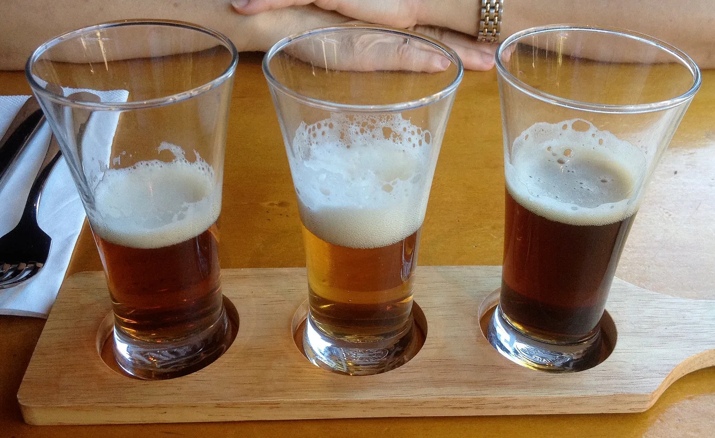 Drei Biergläser mit hellem, bernsteinfarbenem und dunklem Bier auf einem Holzbrett