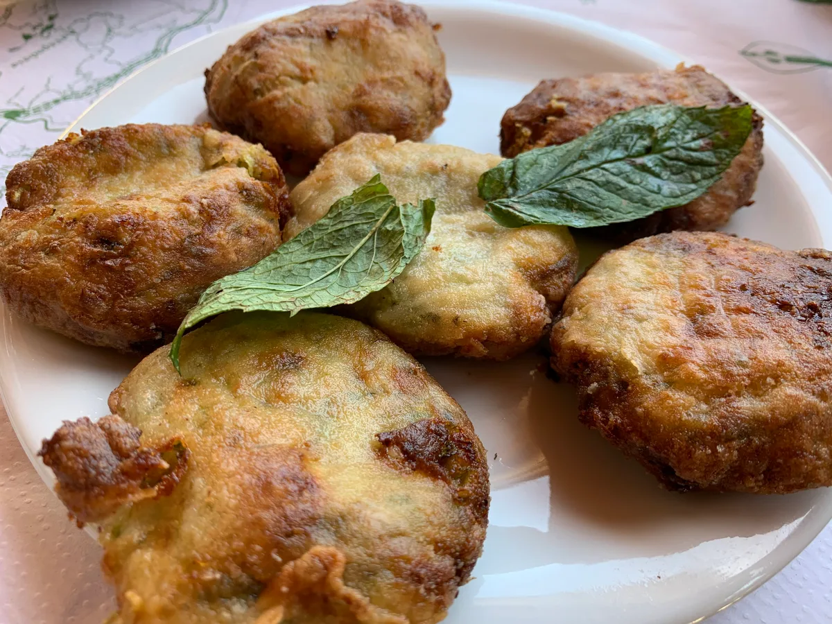Vier goldbraun frittierte Zucchinibällchen mit Minzblättern auf einem weißen Teller