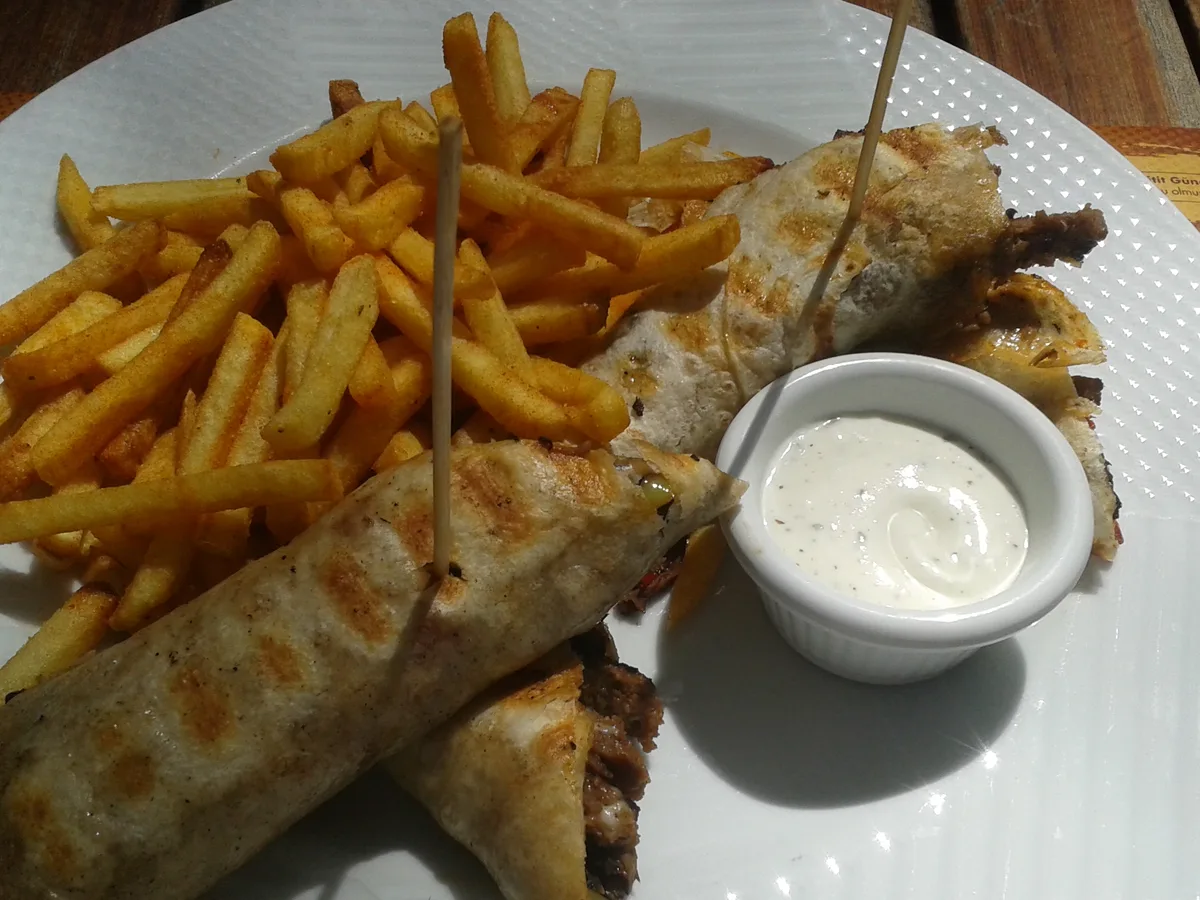 Zwei gegrillte Dürüm-Hälften mit Pommes und einem Schälchen Dip auf einem weißen Teller