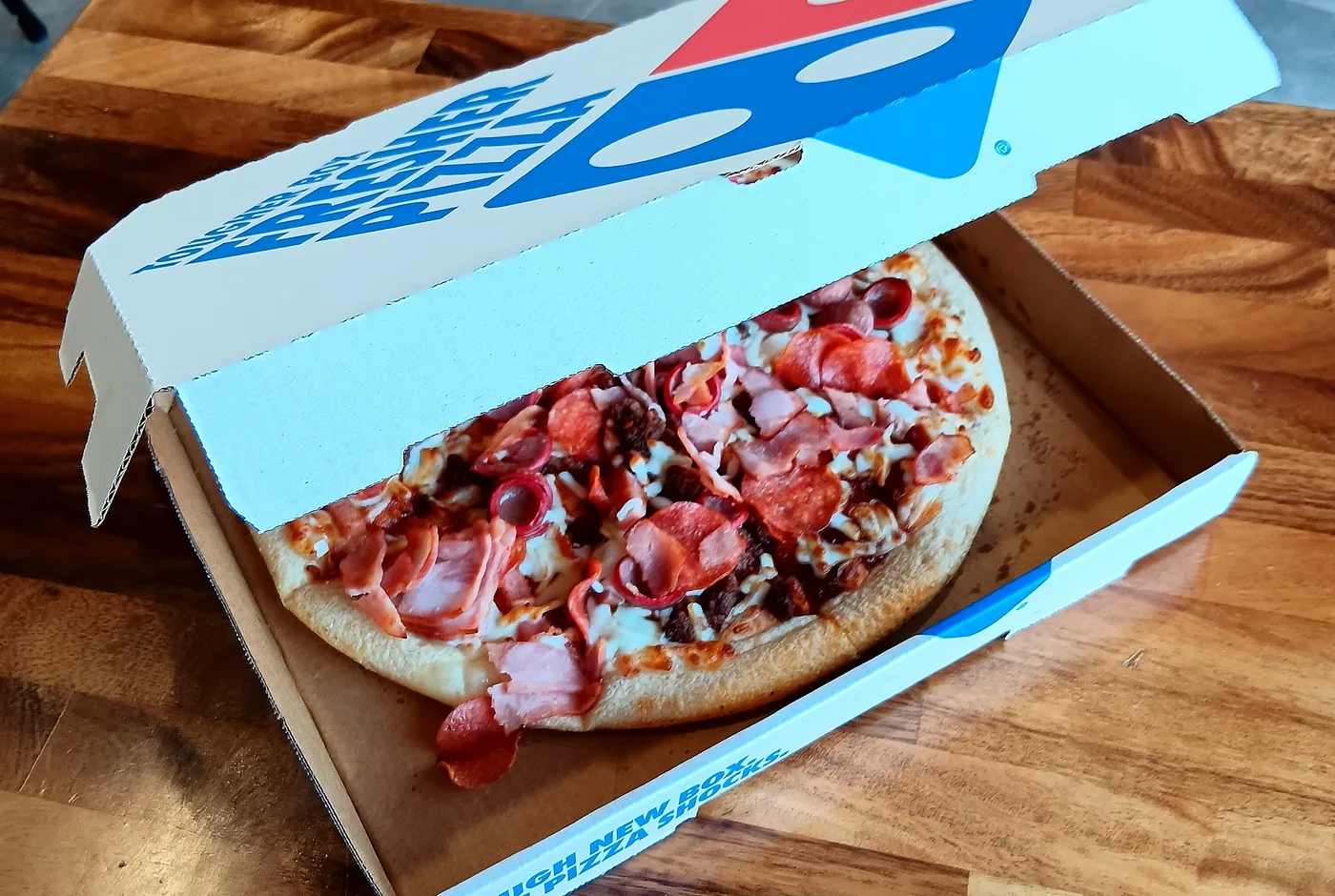 Pizza mit Schinken, Salami und Hackfleisch in einem geöffneten Domino’s-Karton