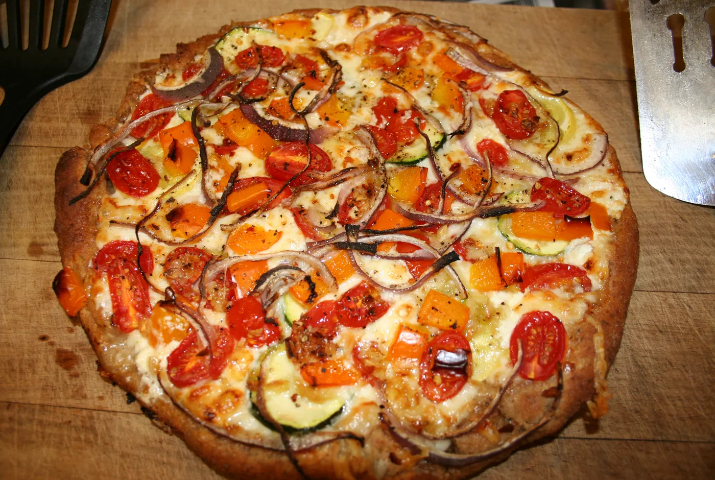 Pizza mit Kirschtomaten, Zucchini, Paprika und roten Zwiebeln auf einem Holzbrett