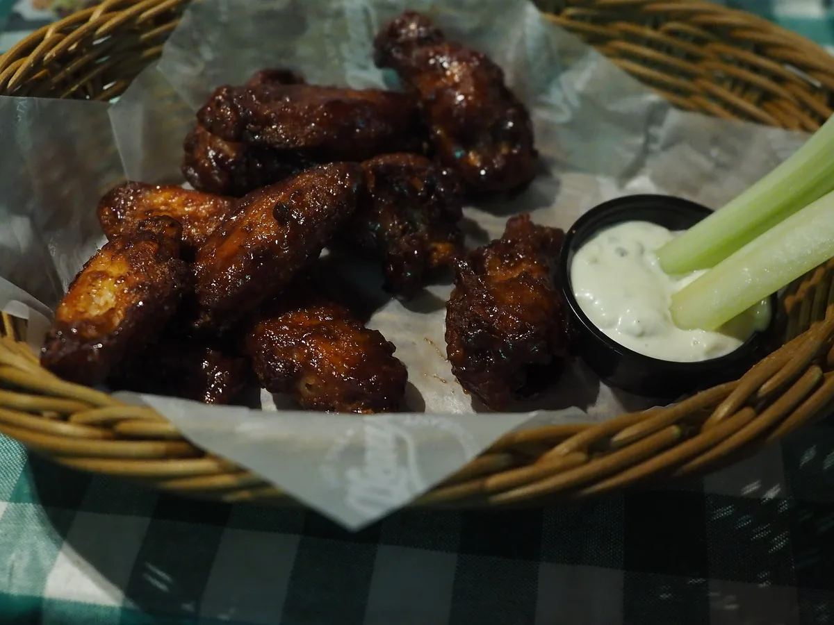 Chicken Wings in einem Korb mit einem Schälchen Dip und Selleriestangen