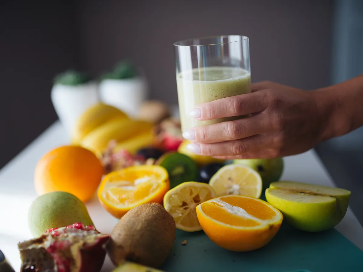 Glas mit frisch gemixtem Smoothie, davor aufgeschnittene Orangen, Kiwi und Äpfel