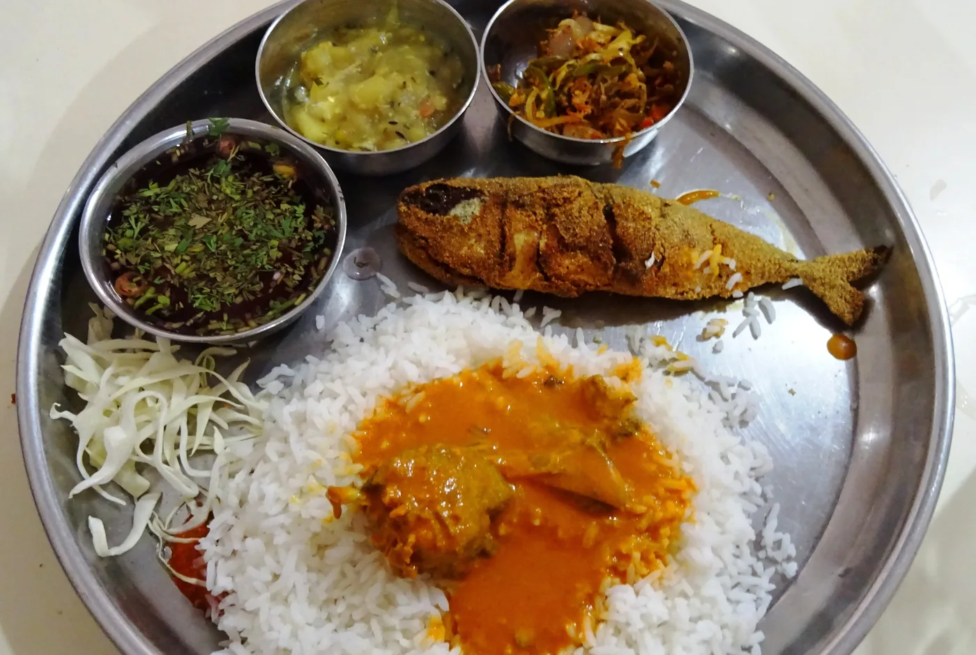Teller mit Fischcurry auf Reis, gebratenem Fisch und mehreren Beilagenschälchen