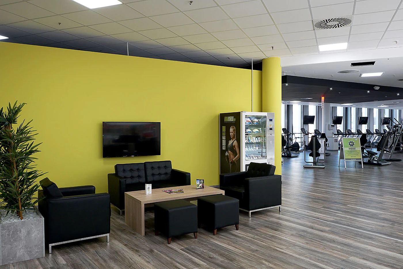 Loungebereich mit Sofas und Fernseher vor gelber Wand