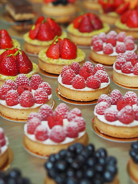 Reihen von Tartelettes mit Erdbeeren, Himbeeren und Blaubeeren auf Vanillecreme, mit Puderzucker bestäubt